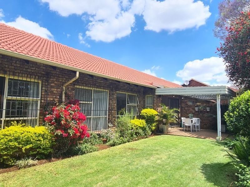 A well-maintained rear exterior view featuring a face brick facade, tiled roof, established garden, and a covered patio area.