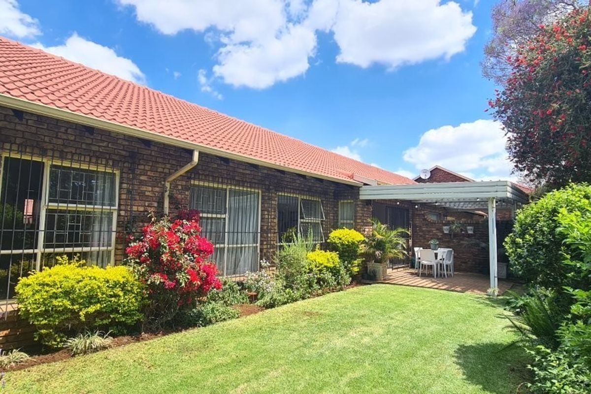 A well-maintained rear exterior view featuring a face brick facade, tiled roof, established garden, and a covered patio area.