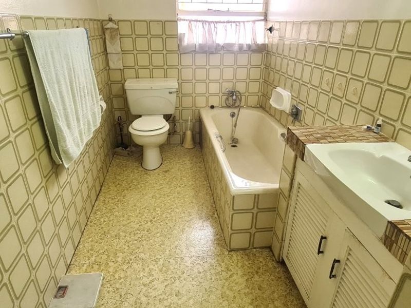 A dated bathroom featuring original wall tiles, a built-in vanity with basin, a standard bathtub, and a toilet.