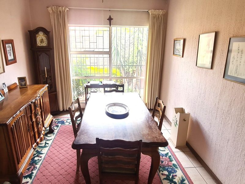 A traditional dining room featuring textured walls, tiled flooring, and a large window with security bars, providing a functional space for family meals.