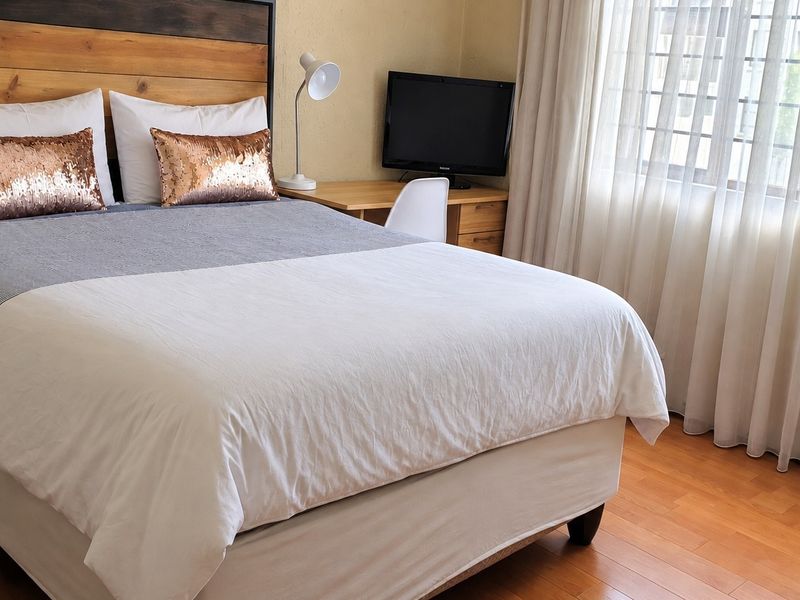 A well-maintained bedroom featuring laminate flooring and large windows with sheer curtains, providing a bright and comfortable living space.