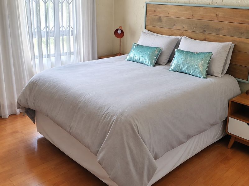 A well-maintained bedroom featuring warm laminate flooring and a large window with security gate, providing a comfortable and functional living space.
