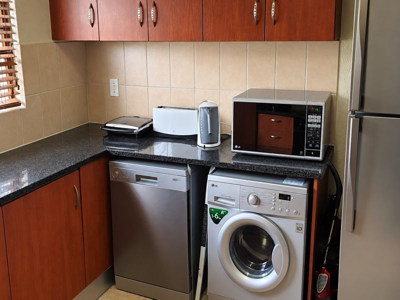 A functional kitchen featuring wood-finish cabinetry, granite countertops, tiled backsplash, and space for integrated appliances including a dishwasher and washing machine.