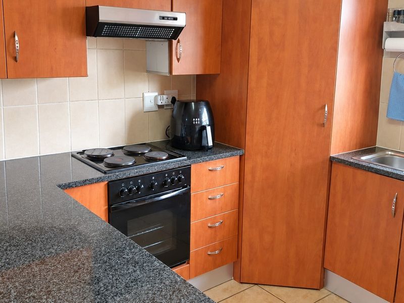 A functional kitchen featuring wood-look laminate cabinetry, granite countertops, a built-in oven with hob, and a stainless steel sink with tiled backsplash.