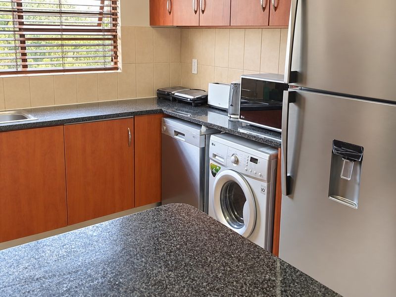 A functional kitchen featuring granite countertops, laminate cabinetry, tiled backsplash, and integrated space for laundry and dishwashing appliances.