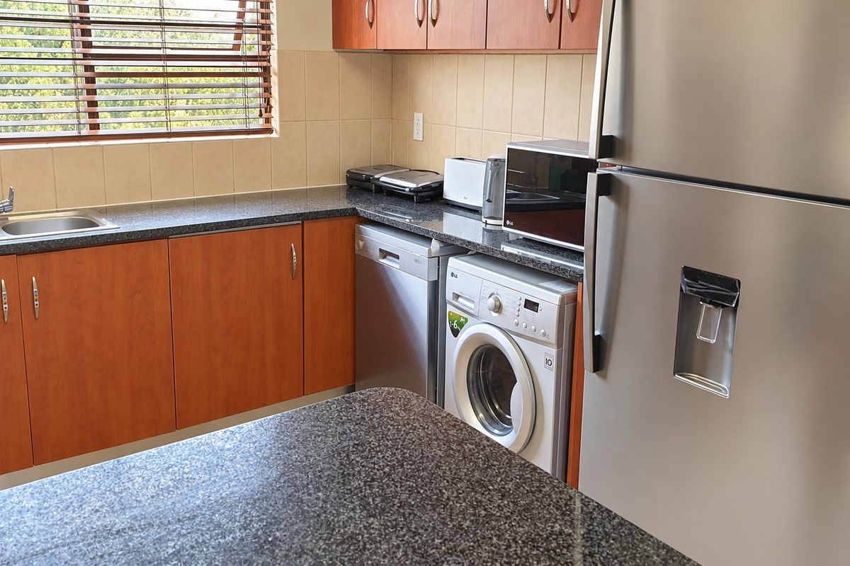 A functional kitchen featuring granite countertops, laminate cabinetry, tiled backsplash, and integrated space for laundry and dishwashing appliances.