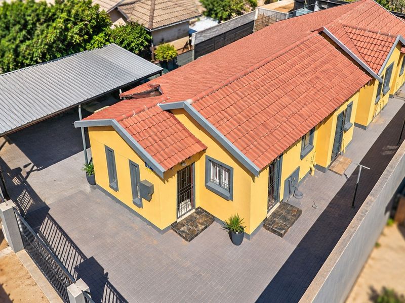 Aerial view of a residential property featuring a yellow facade, terracotta tiled roof, paved driveway, and a covered carport.