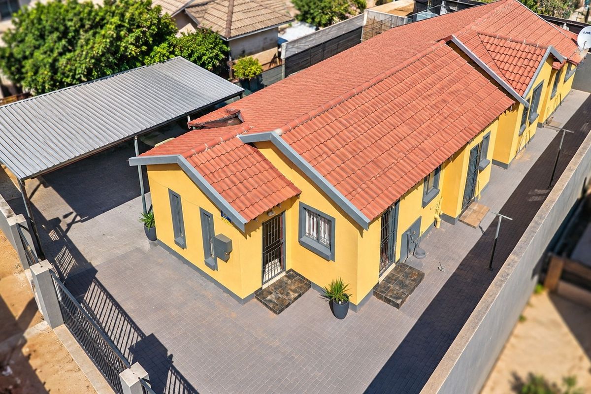 Aerial view of a residential property featuring a yellow facade, terracotta tiled roof, paved driveway, and a covered carport.
