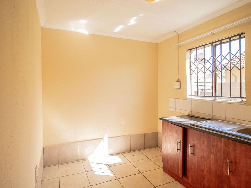 A functional scullery or utility area featuring a stainless steel sink, laminate cabinetry, tiled splashback, and ceramic floor tiles with security window bars.