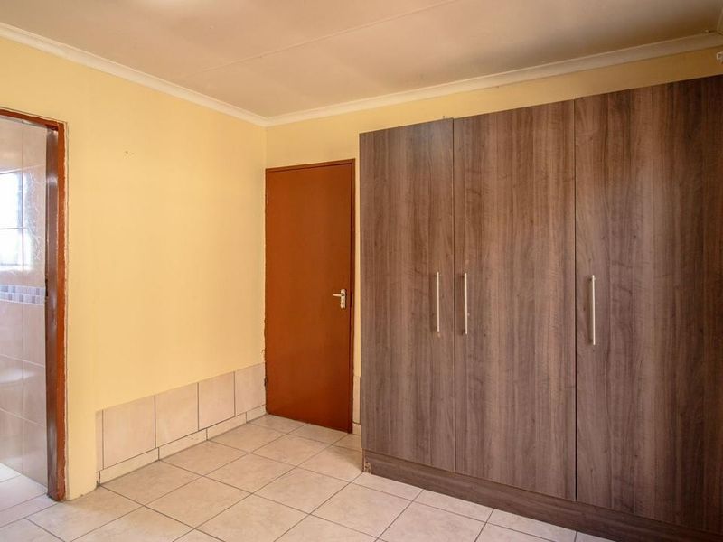 A bedroom featuring built-in cupboards, tiled flooring, and an attached en-suite bathroom with a toilet.