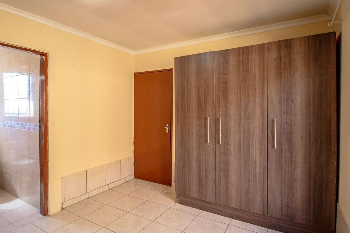 A bedroom featuring built-in cupboards, tiled flooring, and an attached en-suite bathroom with a toilet.
