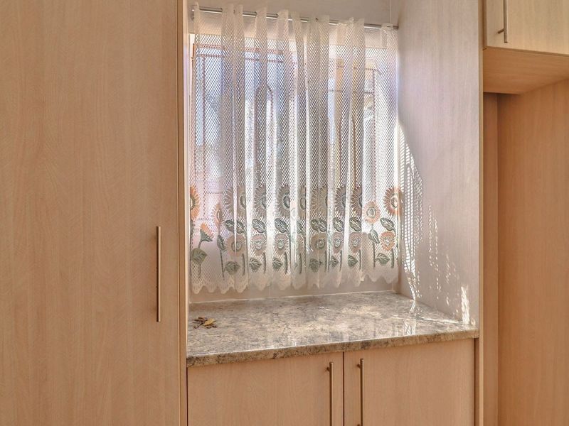 A functional kitchen area featuring light wood-look laminate cabinetry, granite countertops, and a tiled splashback, providing ample storage and workspace.