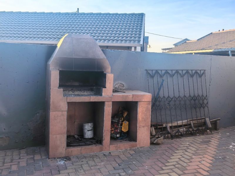 Outdoor patio area featuring a built-in brick braai and paved flooring, enclosed by a boundary wall.
