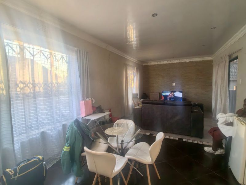 Open-plan living and dining area featuring dark tiled flooring, recessed lighting, and a textured feature wall with visible structural cracking.