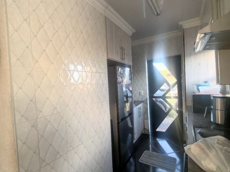 A functional kitchen featuring tiled wall finishes, stone countertops, built-in cabinetry, and an extractor fan, with direct access to the exterior.