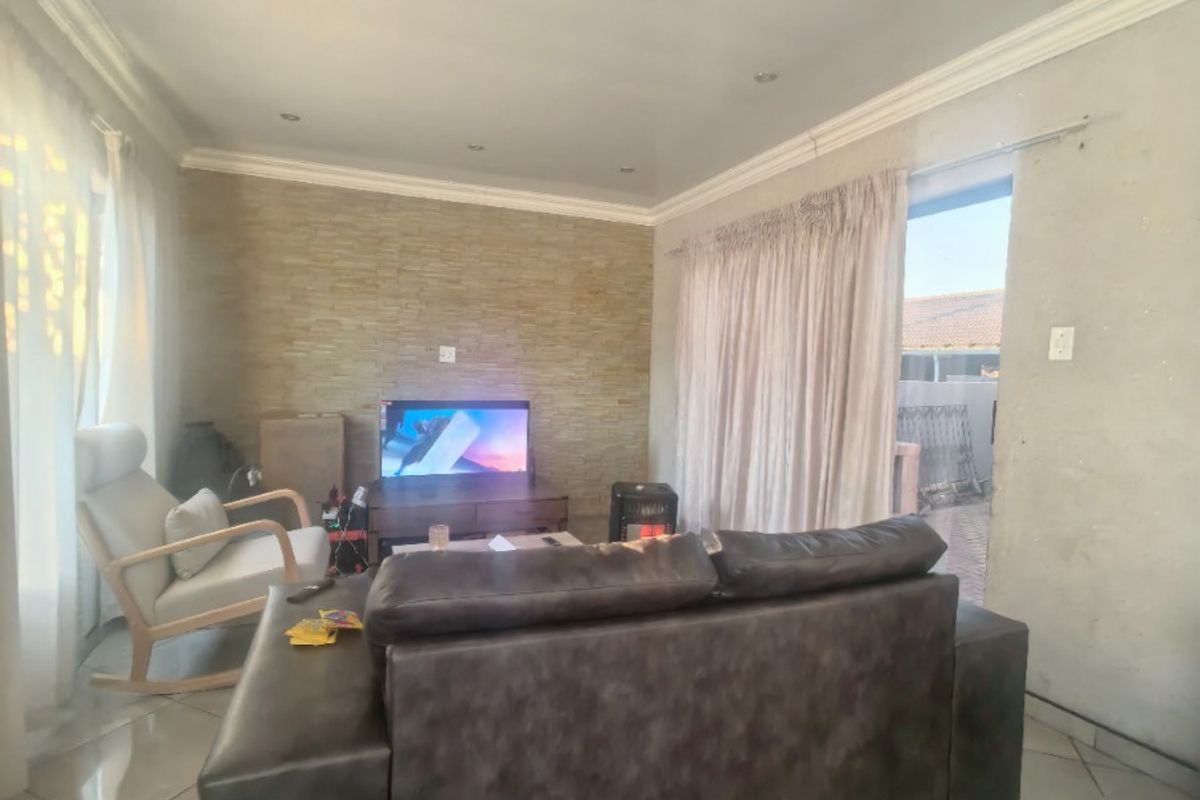 A living room featuring tiled flooring, a stone-clad feature wall, and recessed downlighting, with direct access to an outdoor area via a sliding door.