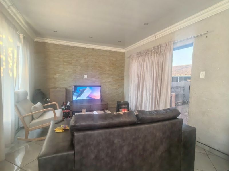 A living room featuring tiled flooring, a stone-clad feature wall, and recessed downlighting, with direct access to an outdoor area via a sliding door.