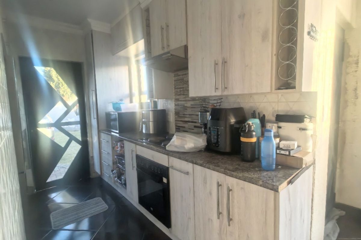 A functional kitchen featuring light wood-finish cabinetry, built-in oven, extractor fan, and dark tiled flooring with a mosaic backsplash.