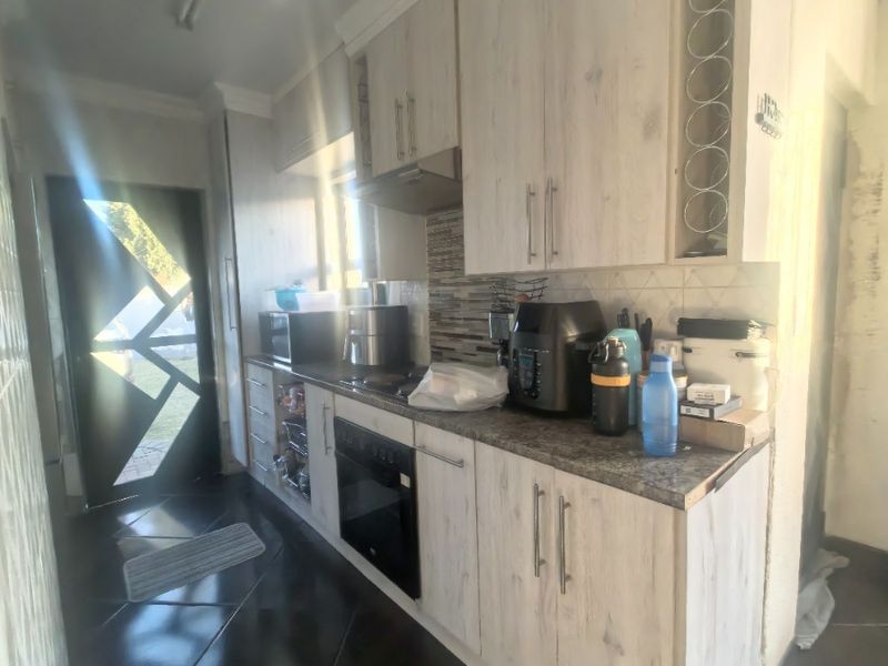 A functional kitchen featuring light wood-finish cabinetry, built-in oven, extractor fan, and dark tiled flooring with a mosaic backsplash.