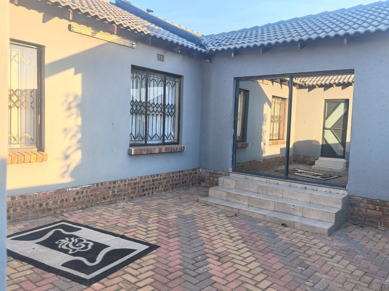 A rear exterior view of the house featuring a paved patio area, sliding glass door access, and security bars on the windows.