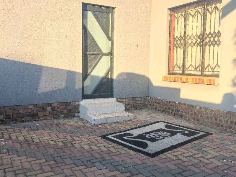 A rear exterior view of the property featuring brick paving, a security gate, and security bars on the window.