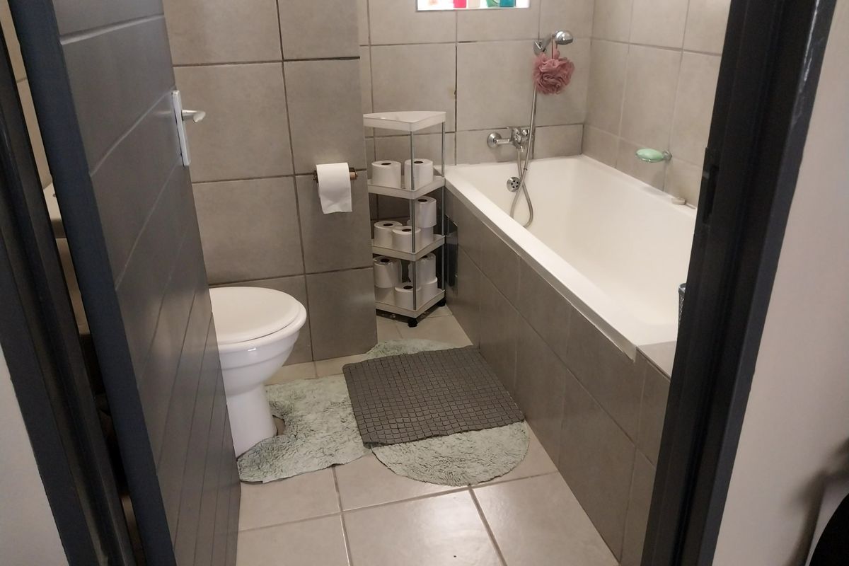 A functional bathroom featuring tiled walls and floors, a standard bathtub with a shower mixer, and a toilet.