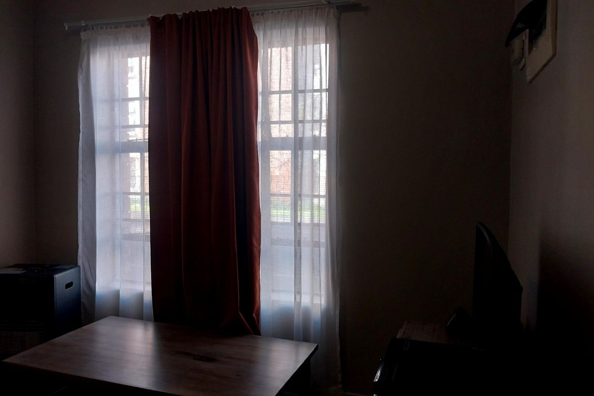 A dimly lit living area featuring sash windows with installed curtain rods, providing natural light to the space.
