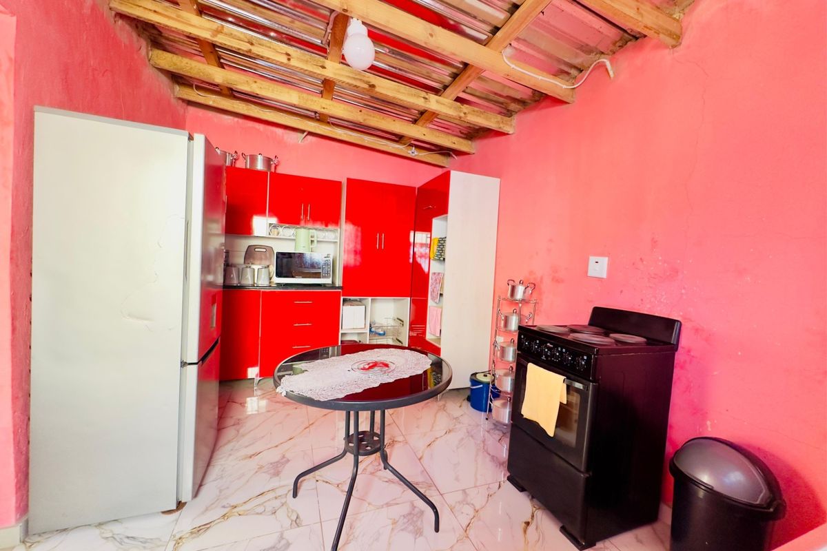 A kitchen area featuring red cabinetry, marble-look floor tiles, and an exposed timber roof structure.