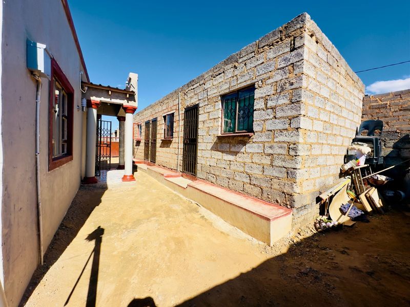 Rear exterior view showing a combination of plastered and unfinished concrete block walls with security gates and bars on windows.