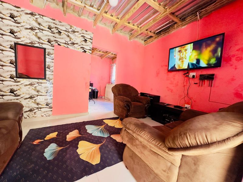 Living room featuring exposed timber roof beams, tiled flooring, and vibrant wall finishes, providing a casual space with direct access to an adjacent room.