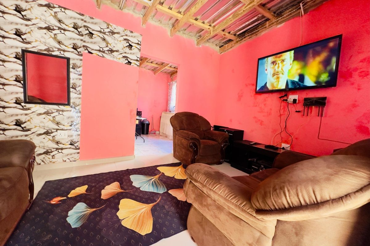 Living room featuring exposed timber roof beams, tiled flooring, and vibrant wall finishes, providing a casual space with direct access to an adjacent room.