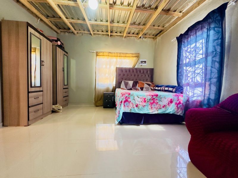 A bedroom featuring tiled flooring and an unfinished exposed timber ceiling, offering a basic layout with potential for aesthetic improvement.
