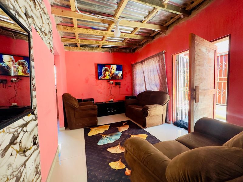 Living room featuring tiled flooring, exposed timber ceiling rafters, and direct access to the exterior via a security gate and timber door.
