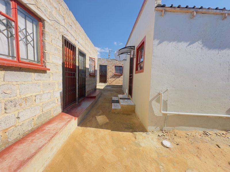 A narrow exterior passage between two residential structures featuring exposed brick and plastered walls with security gates and external plumbing.