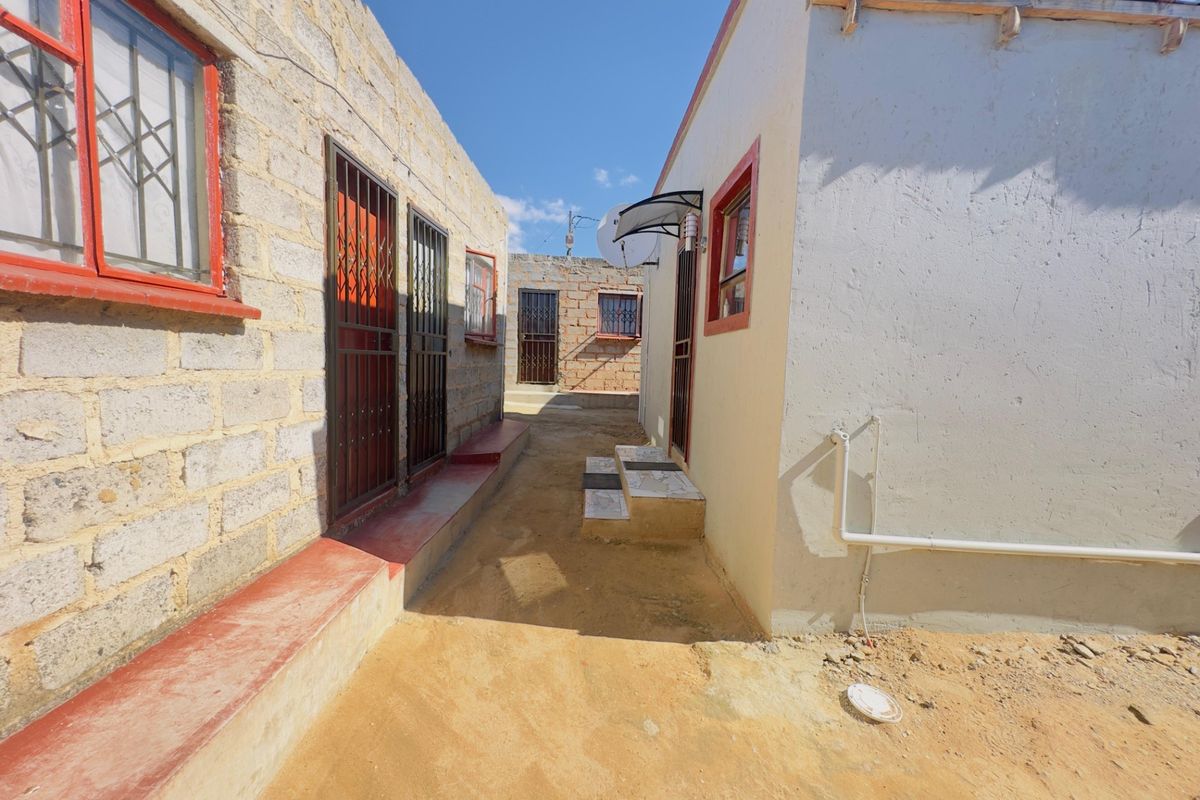 A narrow exterior passage between two residential structures featuring exposed brick and plastered walls with security gates and external plumbing.