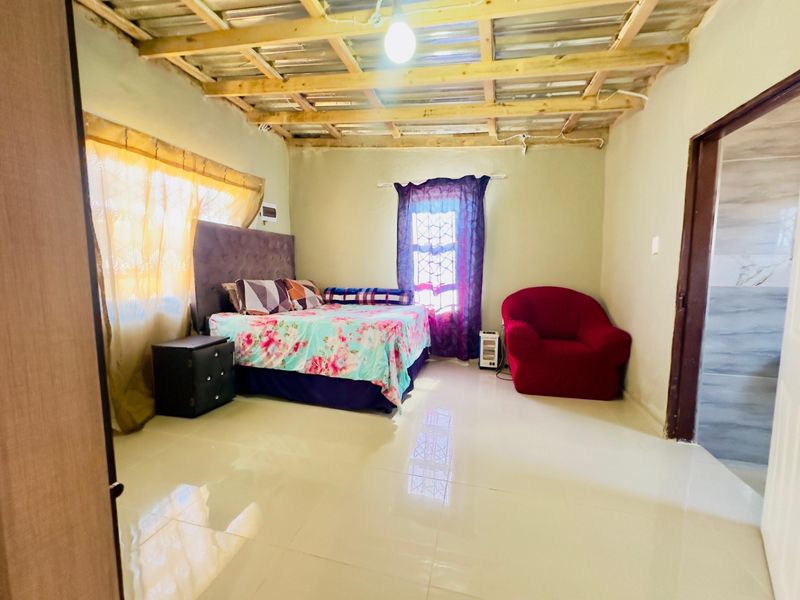 A bedroom featuring tiled flooring and an exposed timber ceiling structure, offering a functional space with potential for aesthetic upgrades and finishing.