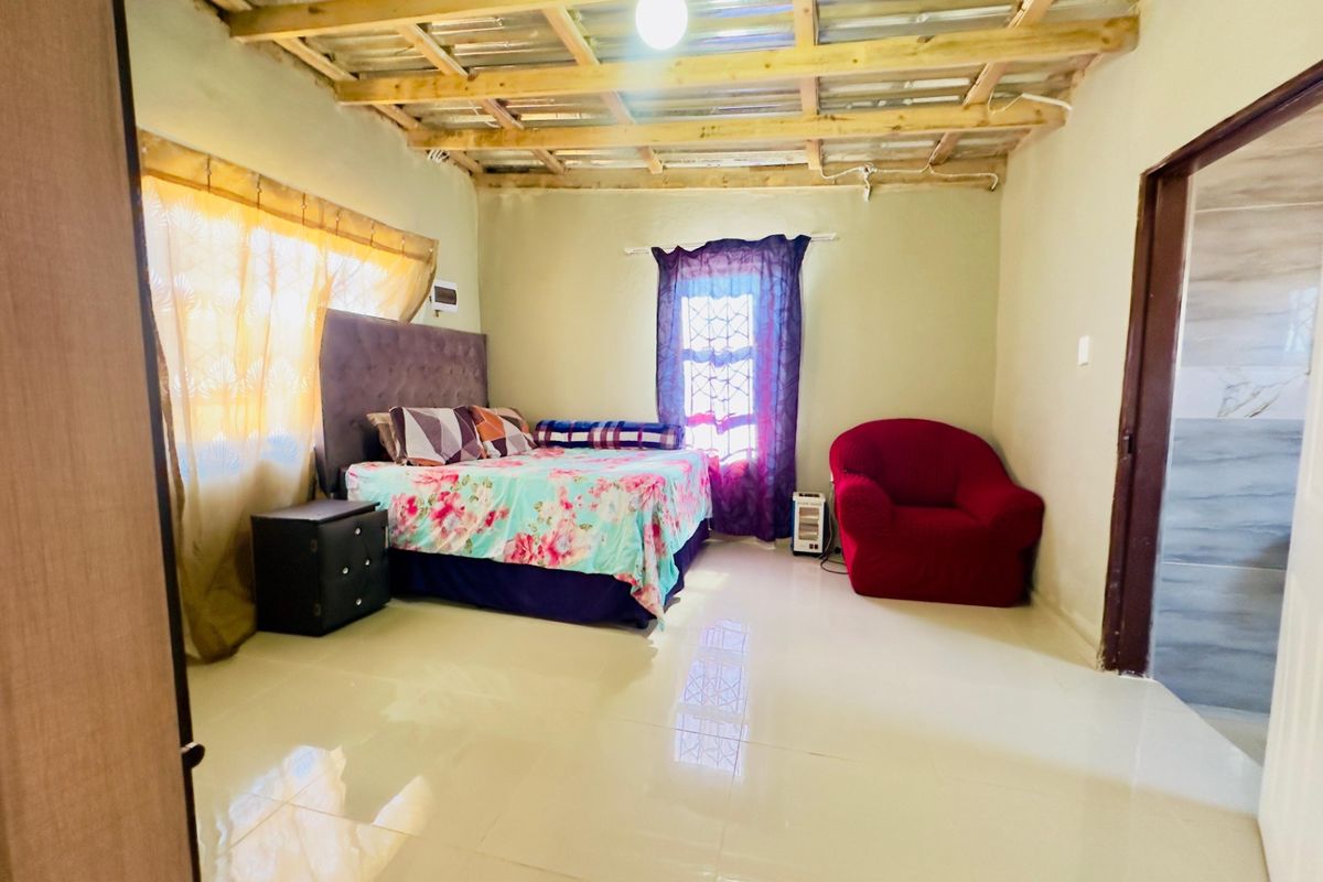 A bedroom featuring tiled flooring and an exposed timber ceiling structure, offering a functional space with potential for aesthetic upgrades and finishing.