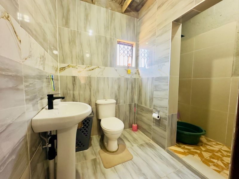 A functional bathroom featuring modern marble-effect wall and floor tiles, a pedestal basin, and a separate shower area with an unfinished ceiling.