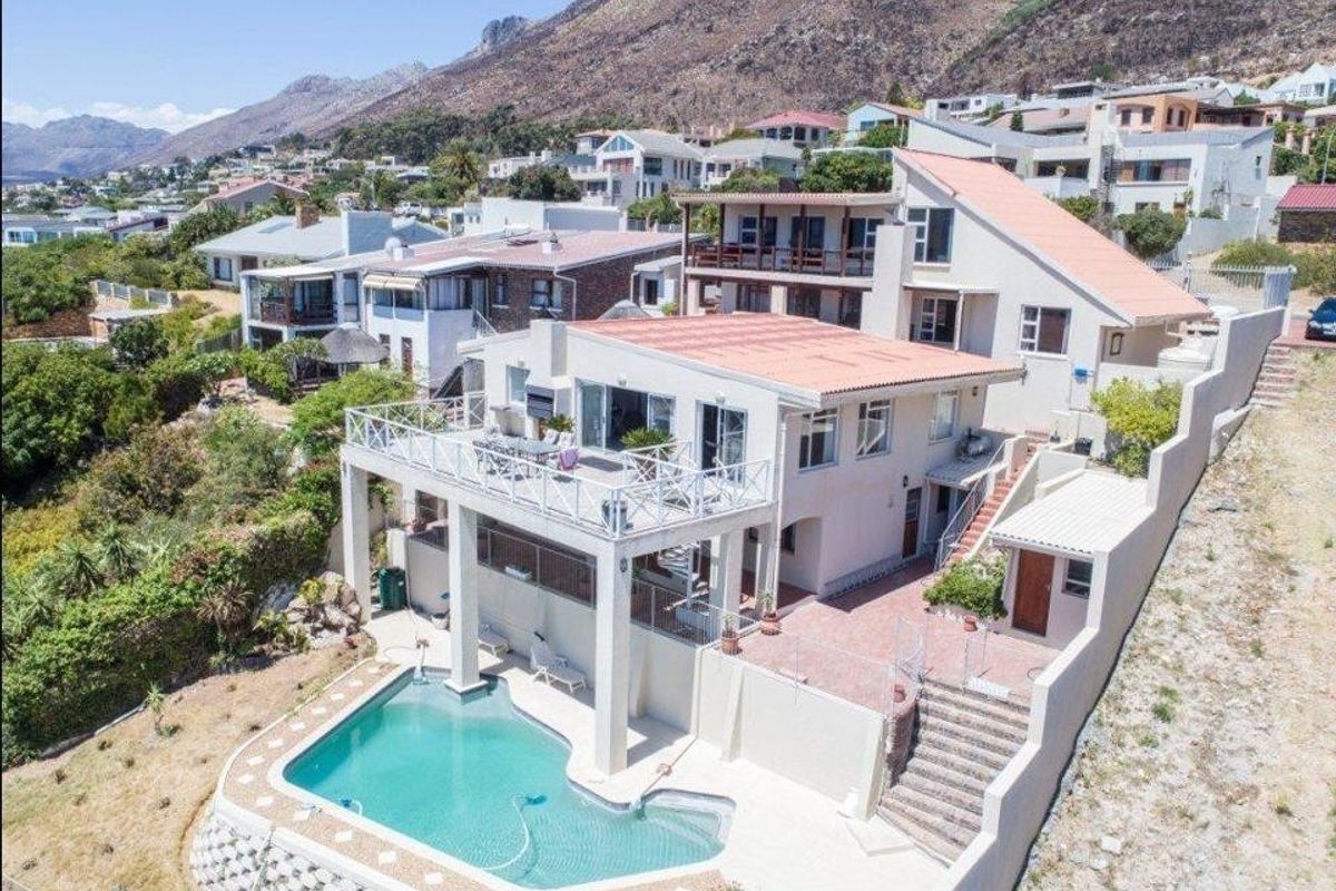 Aerial view of a multi-level guest house featuring a swimming pool, expansive terraces, and balconies with mountain views in a coastal setting.