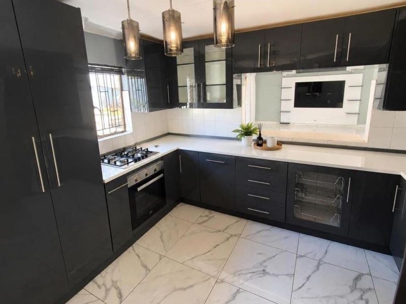 Modern kitchen featuring sleek dark cabinetry, stone countertops, gas hob, built-in oven, and elegant marble-look floor tiles.