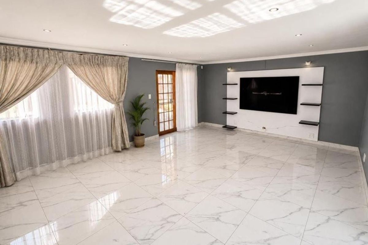 Spacious living room featuring polished marble-look floor tiles, recessed downlighting, and a modern built-in media wall unit with integrated shelving.