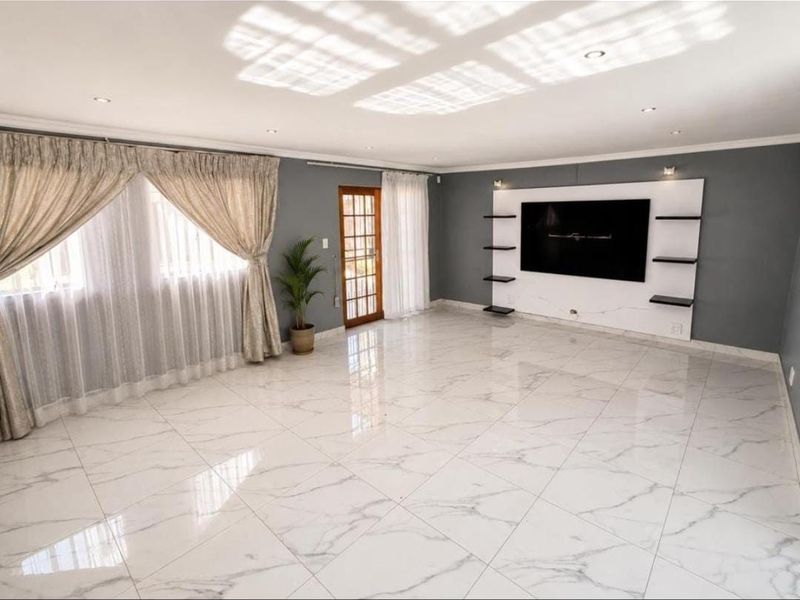 Spacious living room featuring polished marble-look floor tiles, recessed downlighting, and a modern built-in media wall unit with integrated shelving.