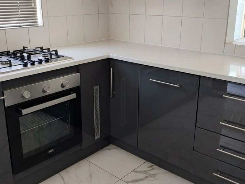 Modern kitchen featuring sleek dark grey cabinetry, white stone countertops, a built-in oven, gas hob, and light-colored floor tiles.