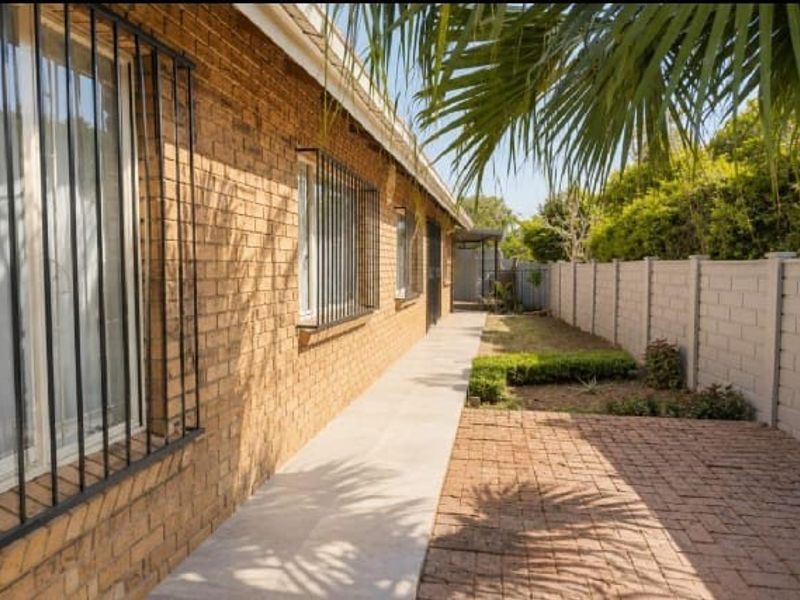 A side view of the property featuring a face brick exterior, security bars on windows, a paved walkway, and a brick-paved patio area.