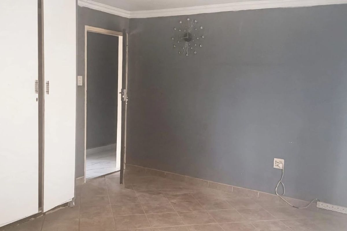 A bedroom featuring built-in cupboards, tiled flooring, and grey painted walls, offering a neutral space ready for personalization.