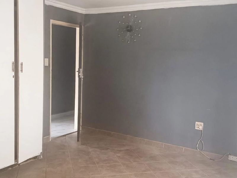 A bedroom featuring built-in cupboards, tiled flooring, and grey painted walls, offering a neutral space ready for personalization.