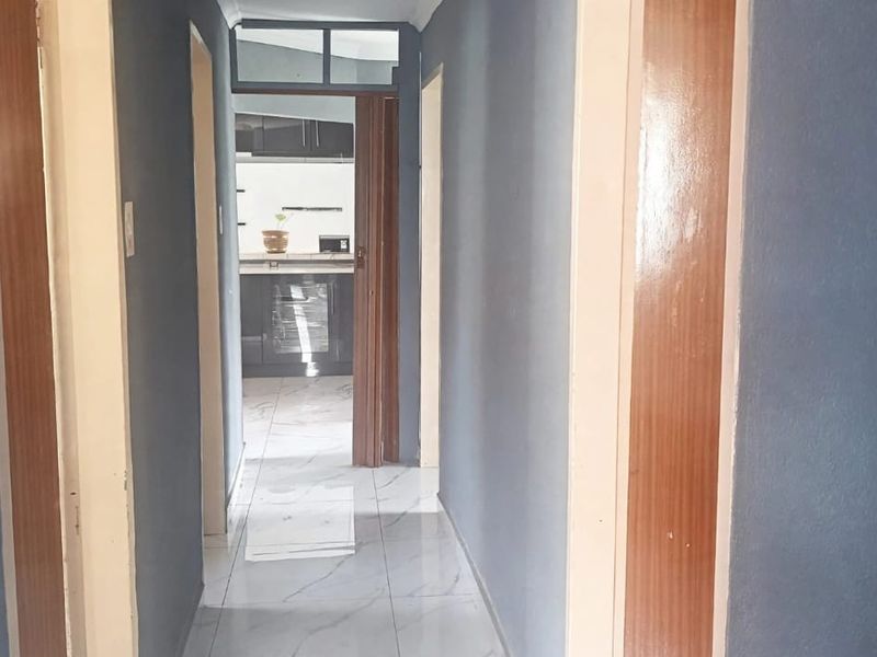 A clean, tiled hallway with wooden door frames leading through to the kitchen area.