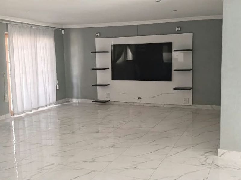 Spacious living room featuring polished marble-look floor tiles, recessed lighting, and a modern built-in media wall unit with integrated shelving.