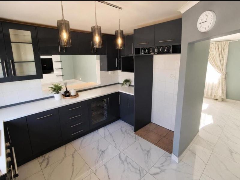 Modern kitchen featuring dark cabinetry, marble-look floor tiles, integrated wine cooler, and stylish pendant lighting, offering a sleek and functional culinary space.