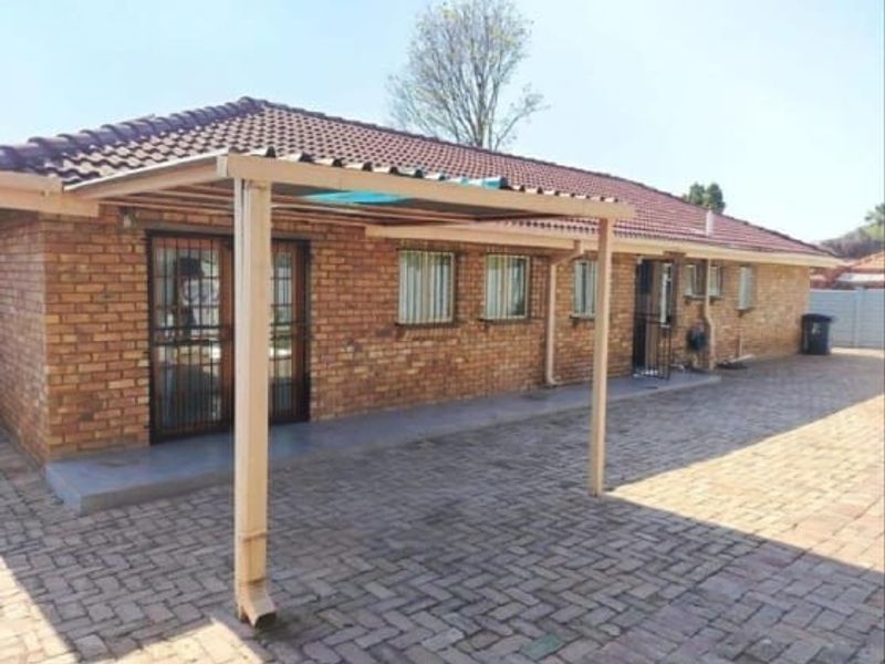Rear view of the house featuring a brick facade, tiled roof, and a covered patio area with paved surroundings.